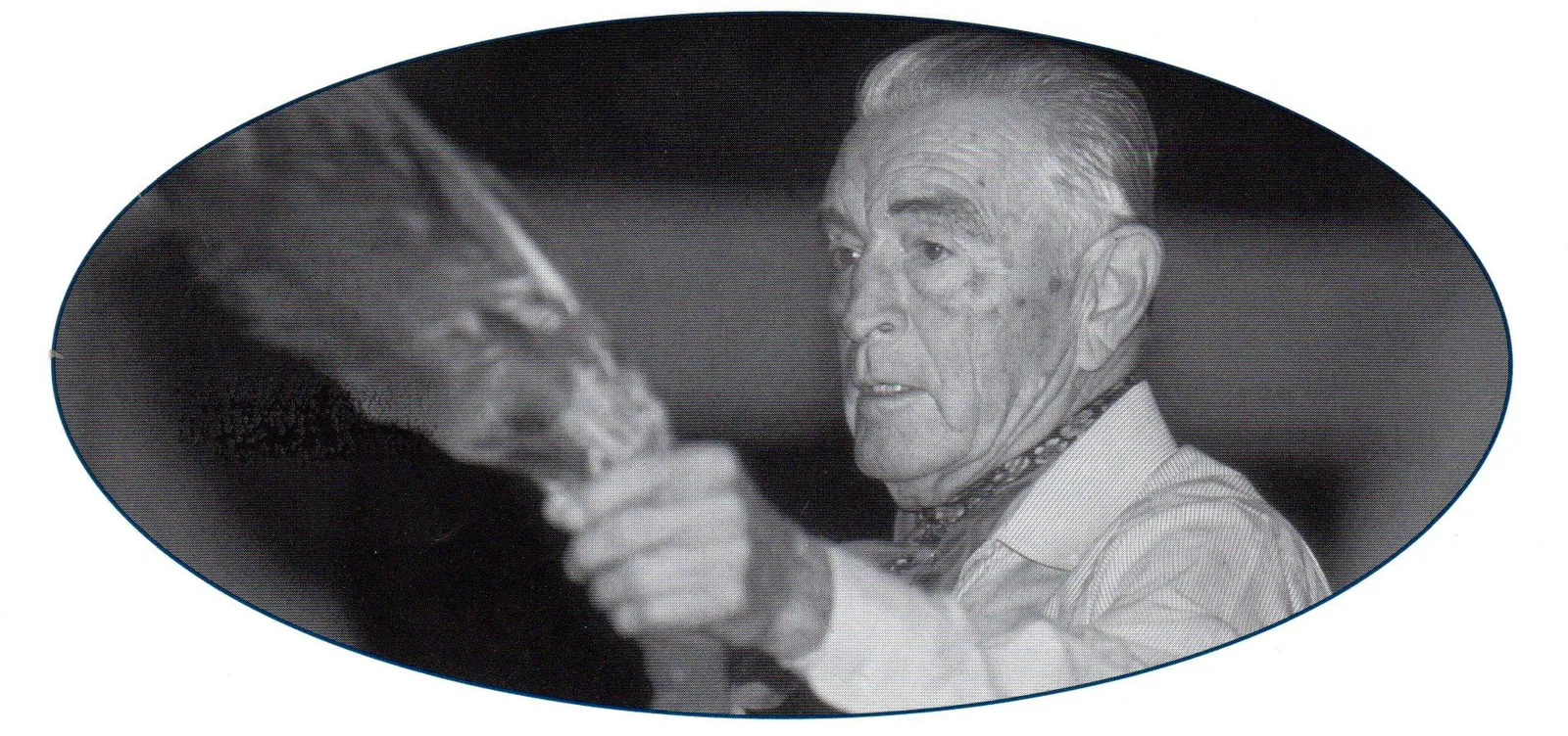 Black-and-white oval portrait of Phil Lane Sr. as an elderly man in a striped shirt and scarf, holding up an eagle feather fan.