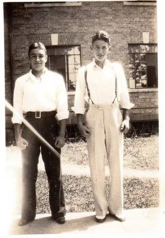 Vintage photo of two young men in white shirts standing in front of a brick building.