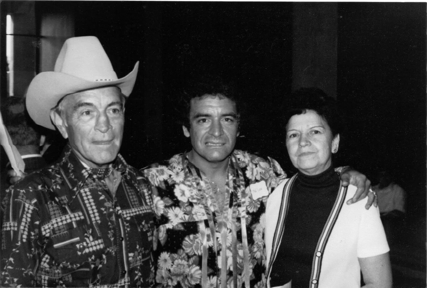Black-and-white photo of an elder in a cowboy hat, a younger man in a floral shirt, and an older woman in a white cardigan.