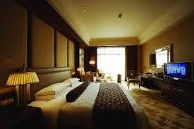 A large hotel bedroom with a wide bed, bedside lamps, a desk with a television, and a window with drapes.