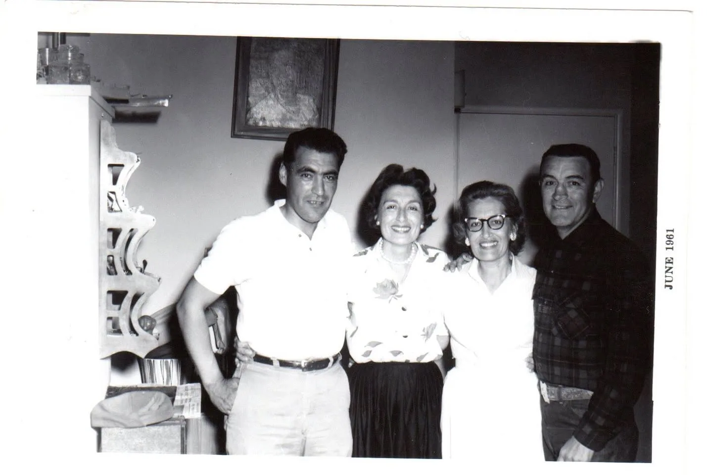 Black-and-white photo dated June 1961 of two men and two women standing arm in arm and smiling in a home.