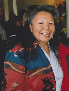 Be'sha Blondin, a smiling Dene elder with gray hair, wearing a colorful red, blue and orange patterned jacket over a white shirt.