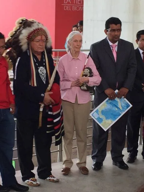 Phil Lane Jr. in a feathered headdress and blanket stands beside Jane Goodall, holding a toy monkey, and Panama's Vice-Minister of the Environment, who holds a map of the sea.