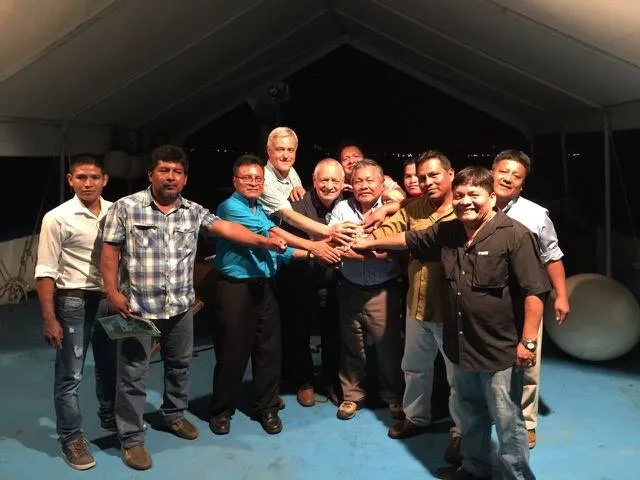 A group of men gathered under a tent at night, reaching their hands together into the center in a gesture of unity after a dinner on a boat in Panama City's harbor.