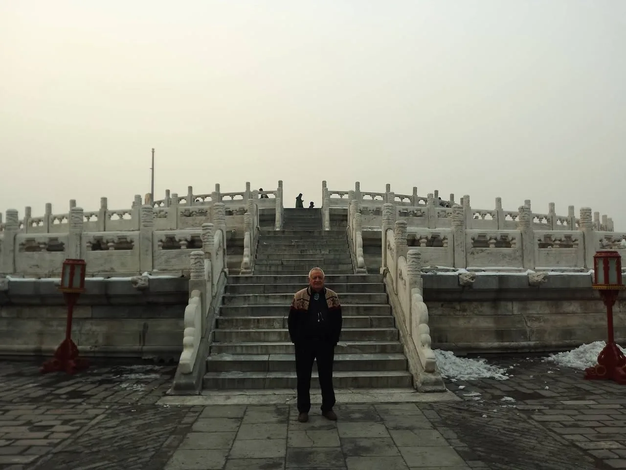Phil Lane Jr. stands at the foot of a wide stone staircase leading up a tiered white marble circular altar at the Temple of Heaven, under a hazy winter sky.