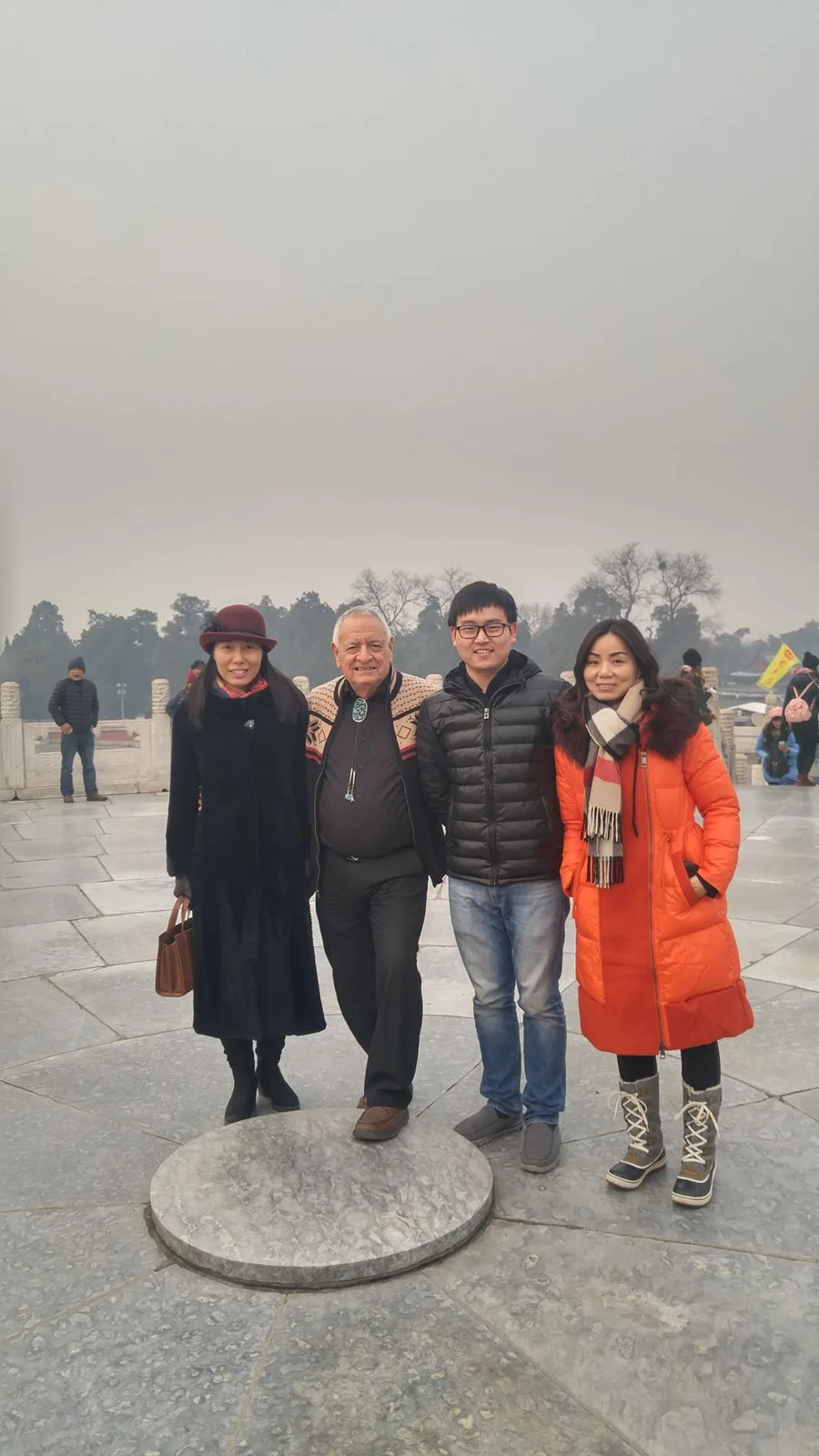 Phil Lane Jr. stands with Ms. Wong, Tonska Dan Young and Ms. Isabella beside the round center stone of the Temple of Heaven altar, all in winter coats.