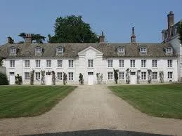 Front facade of a white chateau with dormer windows and chimneys, a gravel drive leading between two trimmed lawns.