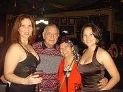 A man with white hair stands among three smiling women at an evening gathering.