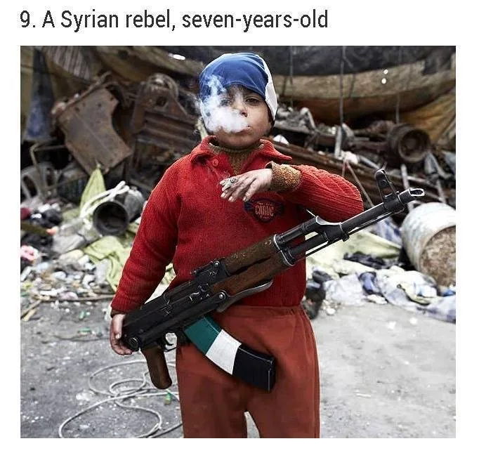 A young boy in a red sweater and blue head scarf exhales cigarette smoke while holding an assault rifle amid rubble and debris. Caption reads: "9. A Syrian rebel, seven-years-old."