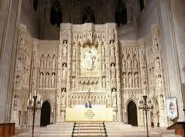 The ornate stone High Altar of the Washington National Cathedral, its carved wall lined with rows of statues of saints around a central relief.