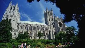 The Washington National Cathedral's Gothic towers rising against a blue sky above gardens where a few visitors walk.