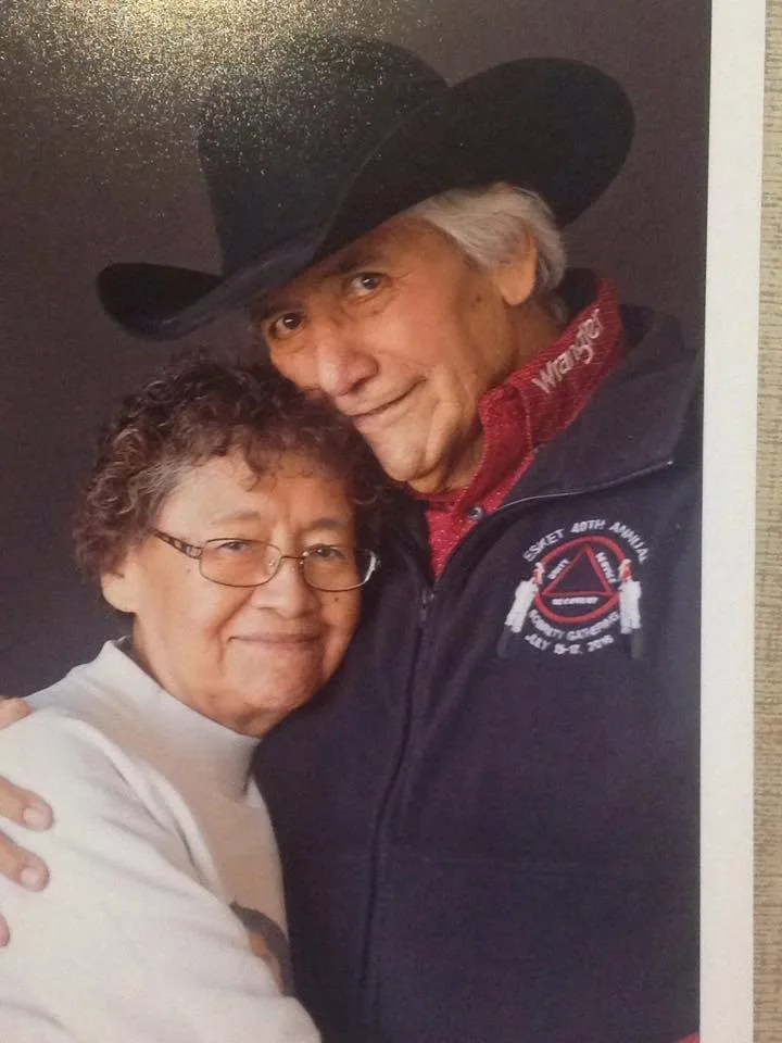 An elderly man in a black cowboy hat and dark jacket with an Esket gathering logo embraces a smiling woman with glasses in a white sweater.