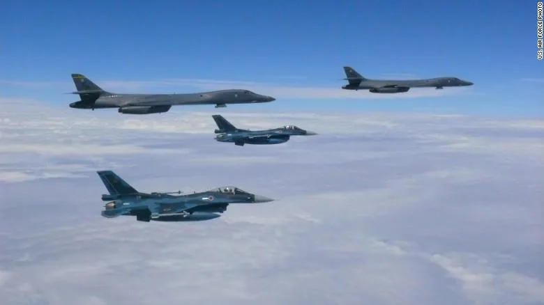 Two grey B-1 bombers fly above a sea of clouds alongside two blue-camouflaged fighter jets, credited as a U.S. Air Force photo.