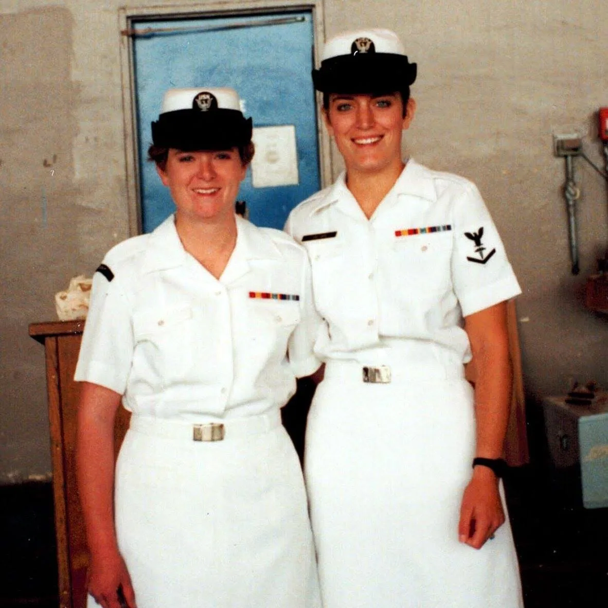 Two smiling women in white U.S. Navy dress uniforms, skirts and black-brimmed caps with ribbons on their chests; Lisa stands on the right.