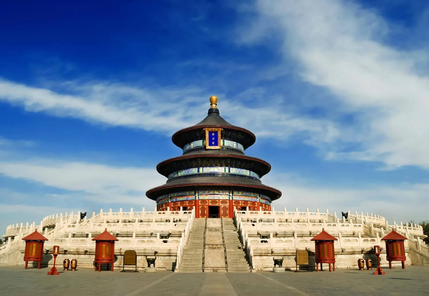 The Temple of Heaven in Beijing, a round three-tiered temple with dark blue roofs and a gold finial, atop white marble terraces with a central stairway under a blue sky.