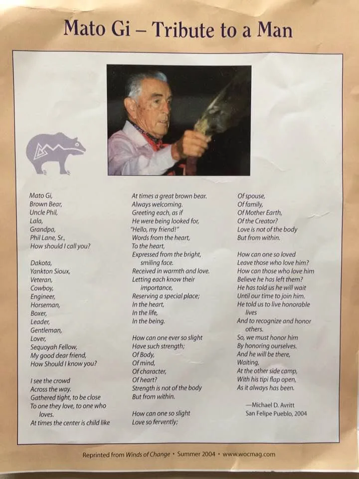 Printed page titled "Mato Gi – Tribute to a Man" with a photo of Phil Lane Sr., an elderly white-haired man holding a feather fan, and a poem by Michael D. Avritt, San Felipe Pueblo, 2004.