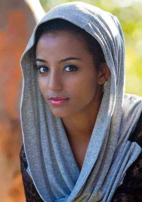 A young woman wearing a gray hooded scarf draped around her head and shoulders gazes calmly at the camera.