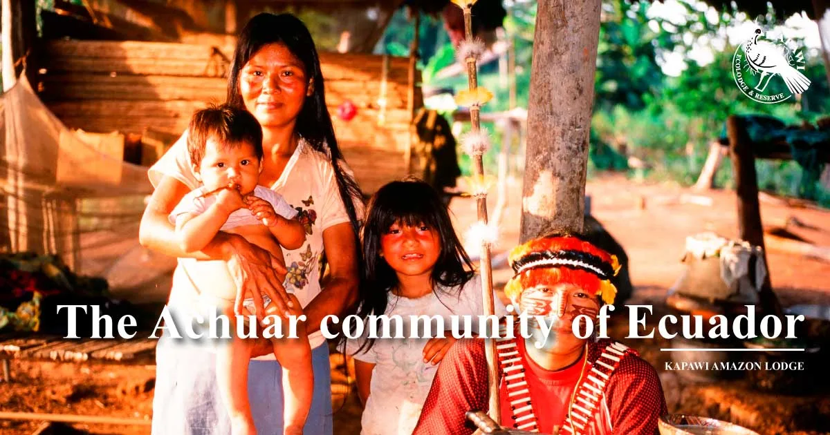 An Achuar woman holding a baby, a young girl, and a man in a feathered headdress and face paint sit in a village. Text reads: The Achuar community of Ecuador, Kapawi Amazon Lodge.