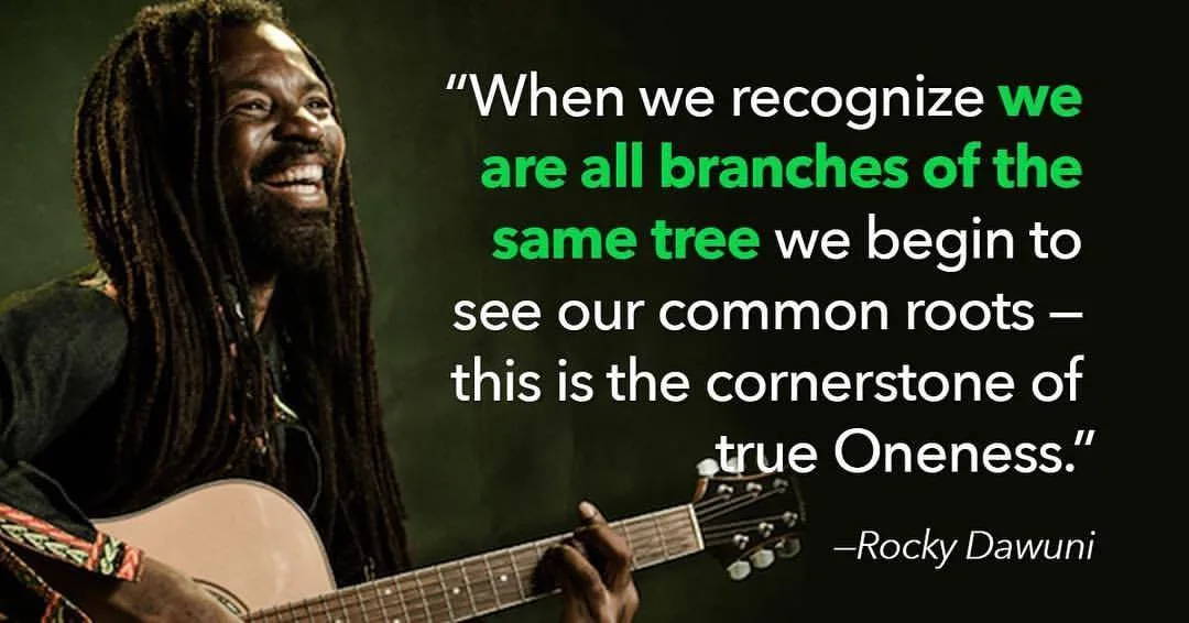Smiling musician with long dreadlocks, identified as Rocky Dawuni, playing an acoustic guitar beside his quote: when we recognize we are all branches of the same tree, we see our common roots, the cornerstone of true Oneness.