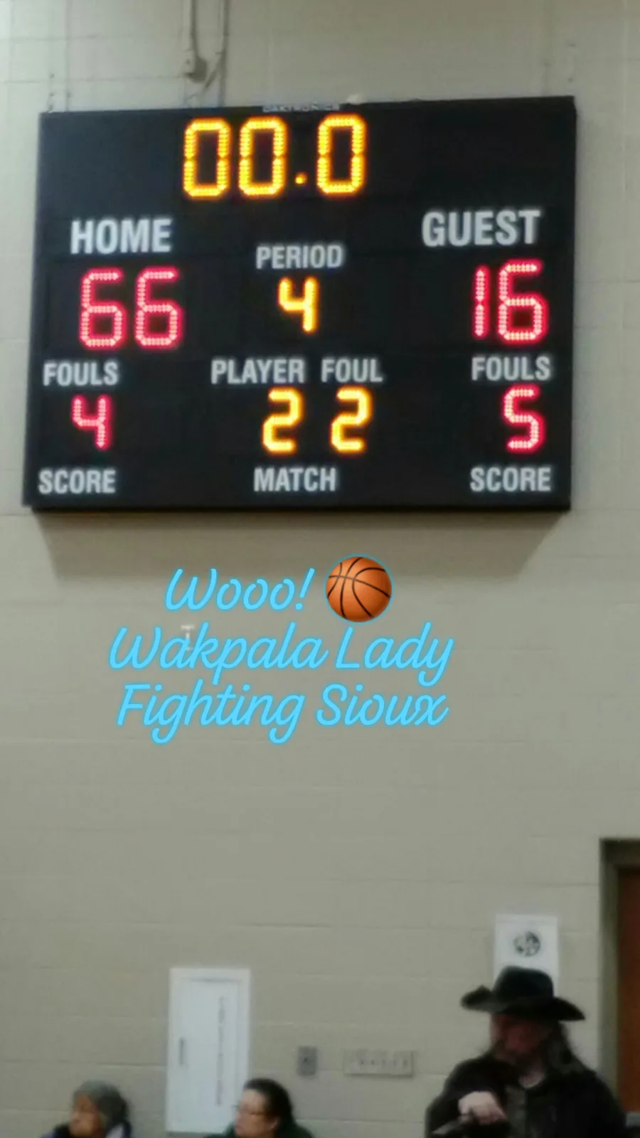 A gym scoreboard showing a final score of Home 66, Guest 16 in the fourth period, with the overlaid words "Wooo! Wakpala Lady Fighting Sioux" and spectators seated below.