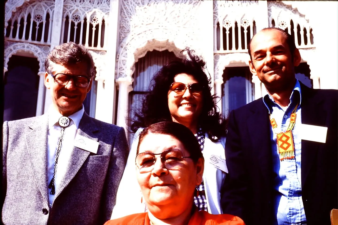 Four smiling people wearing name tags pose in front of an ornate white temple facade.