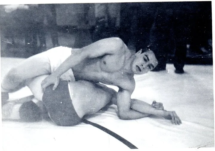 Black-and-white photo of a wrestler pinning an opponent on the mat during a match.