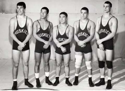 Five young wrestlers in Huskies singlets stand side by side on a mat.