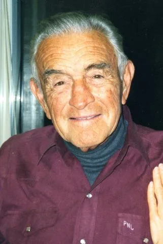 Portrait of a smiling elder with gray hair in a maroon shirt.