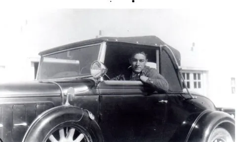 Vintage photo of a young man sitting in a classic convertible car.