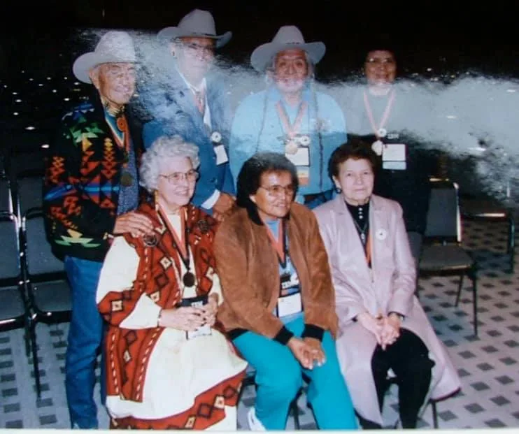 Seven elders wearing medals posing together, four standing and three seated.