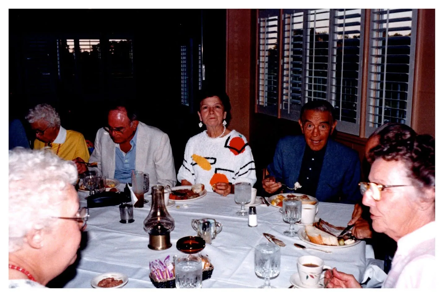 A group of older adults sharing a meal at a table with a white tablecloth.
