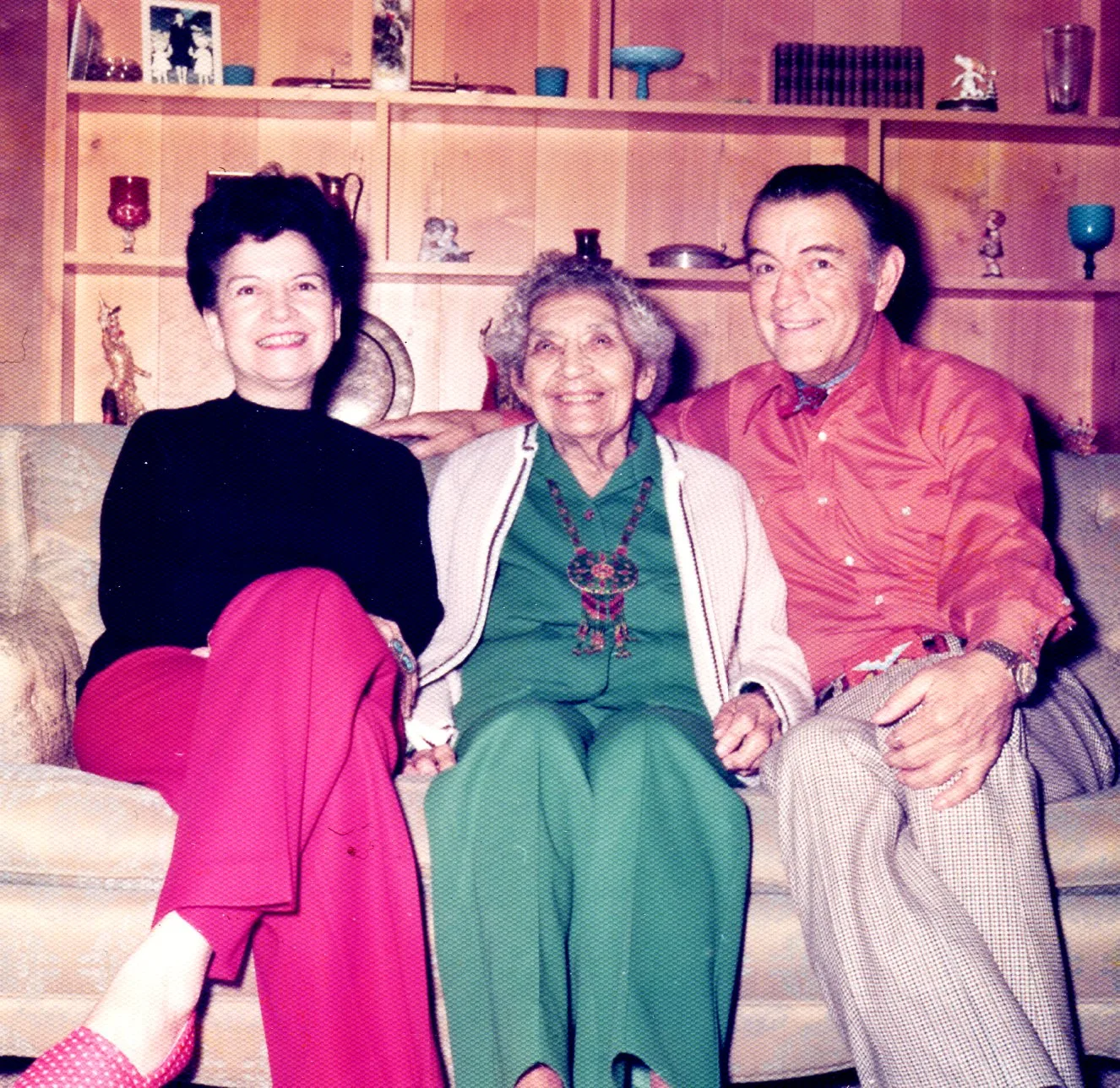 Two smiling adults on a sofa with an elderly woman in green between them.
