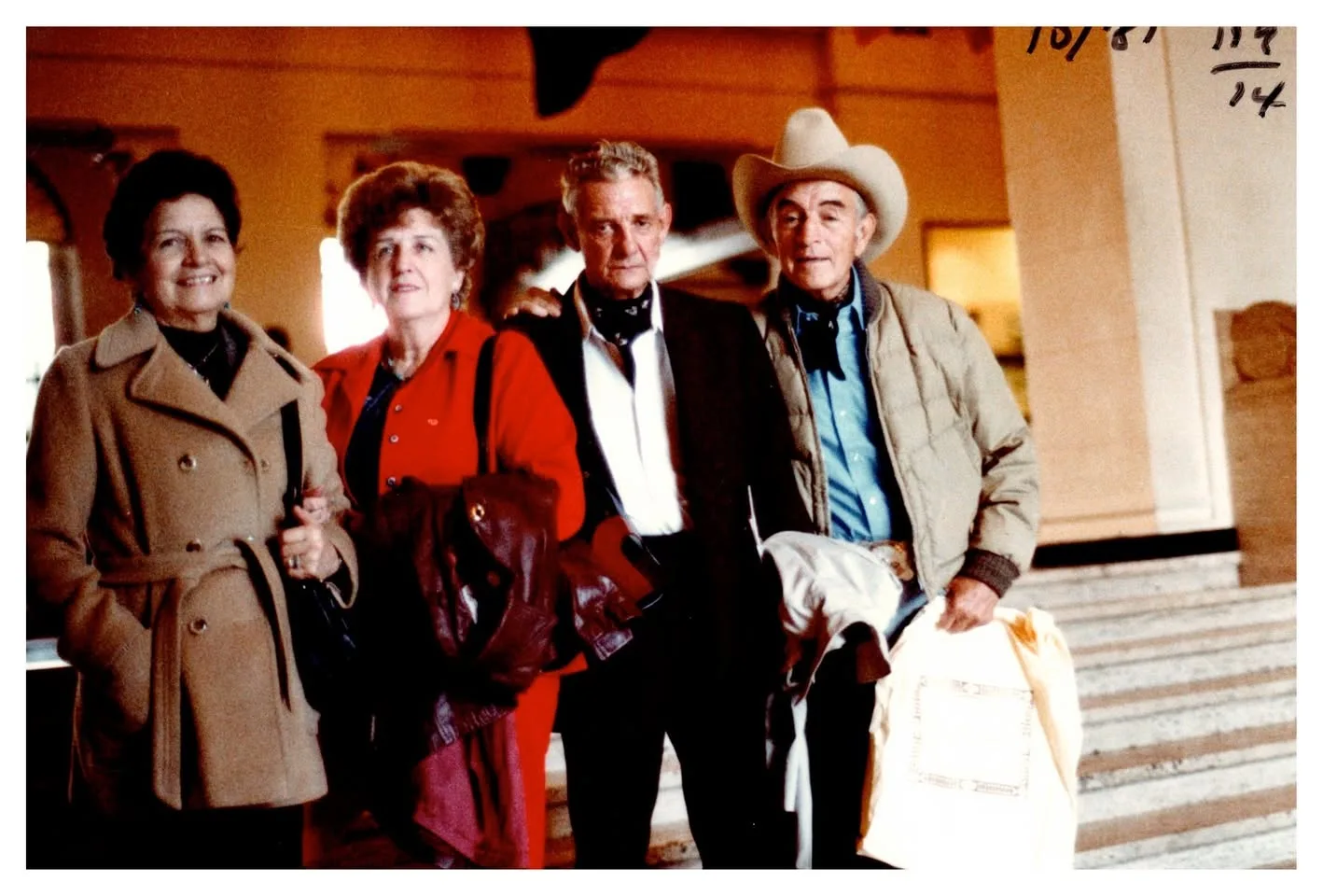 Two women and two men in coats standing together in a hall, one man in a cowboy hat; dated 10/81.