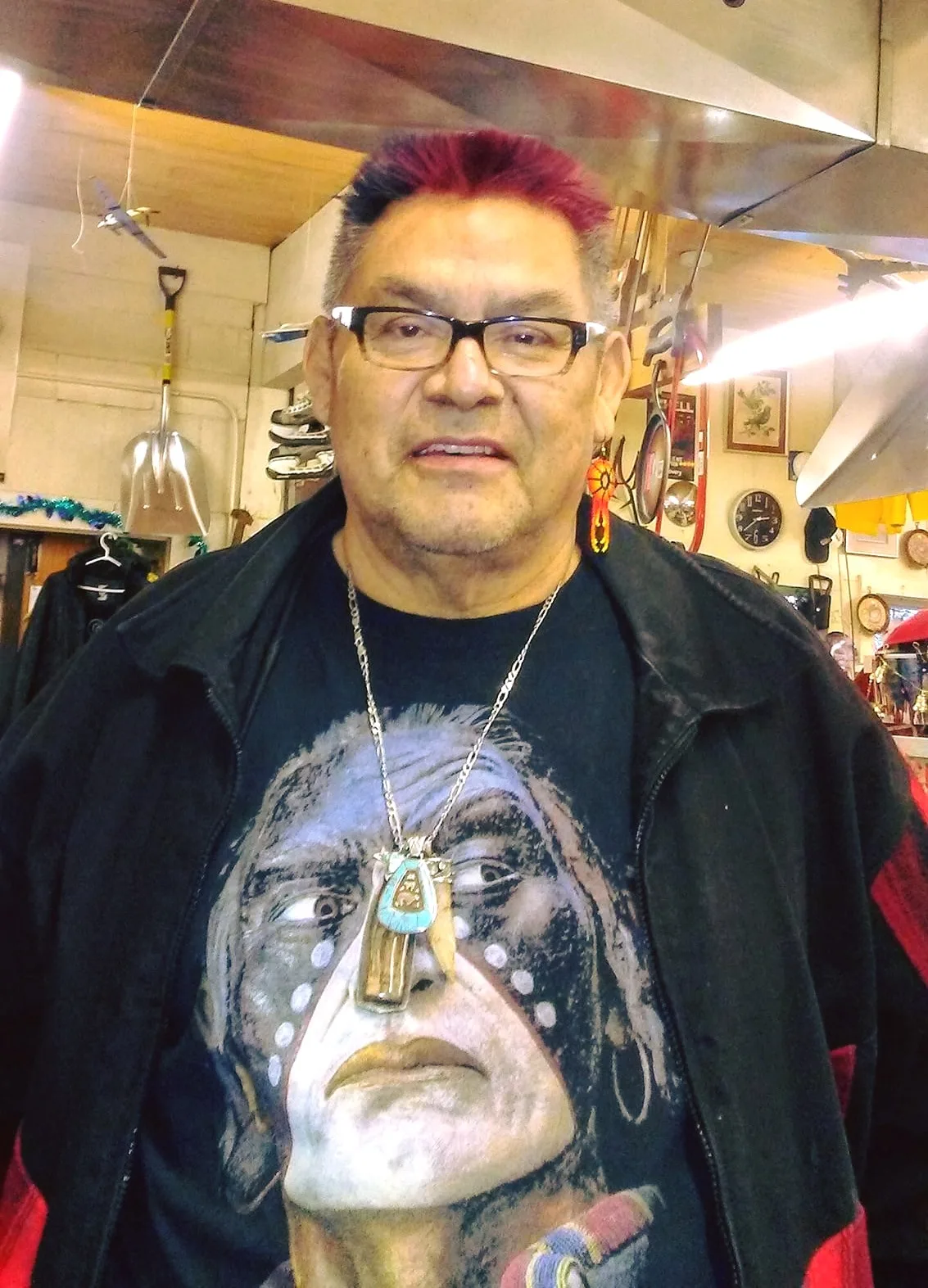 Howard Vincent, with red-dyed hair and glasses, wearing a black jacket over a T-shirt with a painted Indigenous face, a silver pendant and beaded earring.