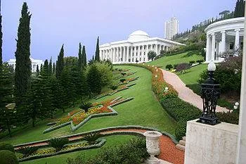 Terraced gardens on Mount Carmel in Haifa, with manicured lawns, flower beds, tall cypress trees and white colonnaded buildings with a dome.