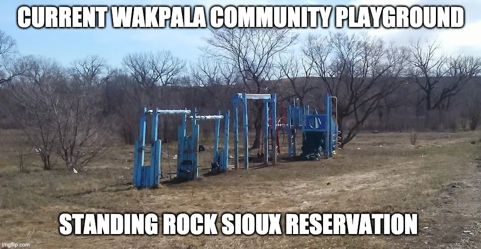 Worn, faded blue playground equipment standing in dry brown grass among bare trees, captioned "Current Wakpala Community Playground, Standing Rock Sioux Reservation."