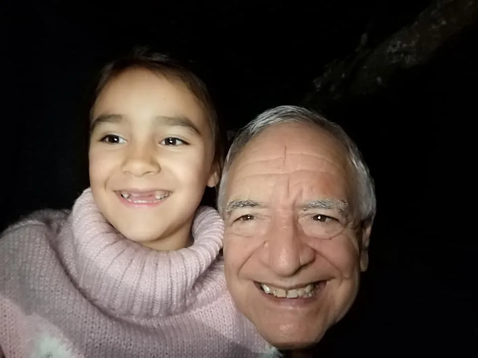 Close-up night selfie of a smiling young girl in a pink knit sweater cheek to cheek with a smiling white-haired elder.