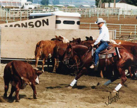 An older man in a white cowboy hat and white shirt rides a chestnut quarter horse in a dusty arena, cutting a red calf away from a herd of cattle.