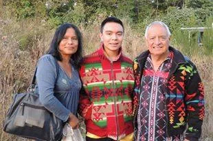 A woman with a shoulder bag, a young man in a red patterned sweater and a white-haired elder in a patterned jacket stand together outdoors.