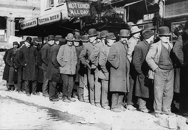 Historic black-and-white photograph of a long line of men in overcoats and bowler hats waiting on a snowy sidewalk beneath signs reading "Hot Lunch All Day" and "Extra Beer."