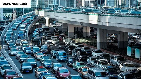 Dense traffic jam of cars, taxis and buses packed bumper to bumper on a multi-lane city road beneath a crowded elevated highway.
