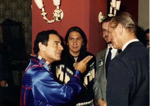 Phil Lane Jr. and Chief Leonard George, one in a blue ribbon shirt and one in fringed regalia, speak with Prince Philip in Assisi in 1986 as Hugh Locke looks on.