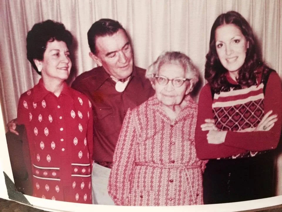A vintage family photograph of Unchi Martina, a white-haired elder in glasses, standing with Phil's mother, father and sister Deloria before a curtain.