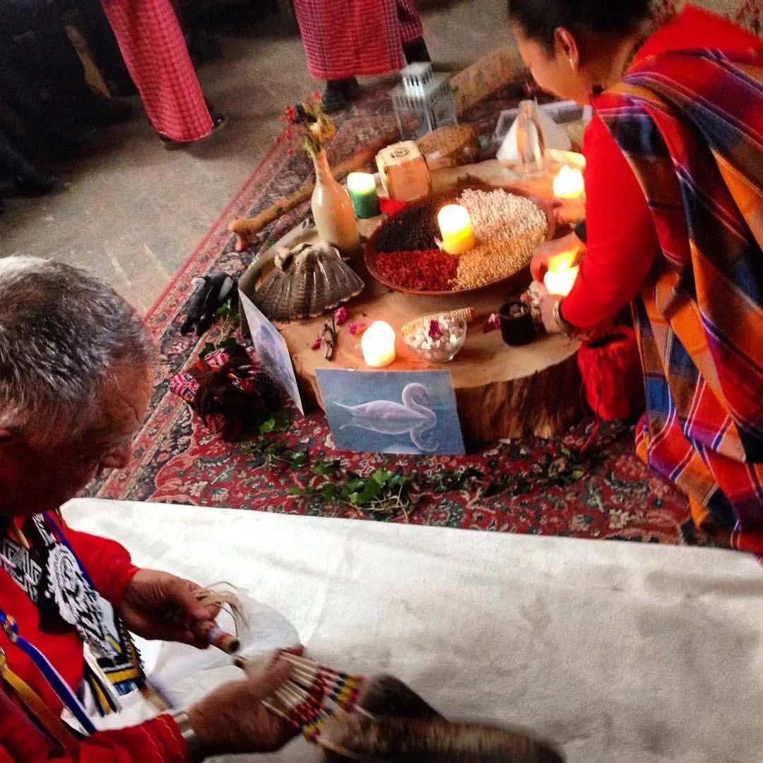 Janet Dolera, in a red and orange plaid shawl, lights candles on an altar of seeds, flowers and a swan picture, while Chief Phil Lane Jr. holds a beaded eagle feather fan.
