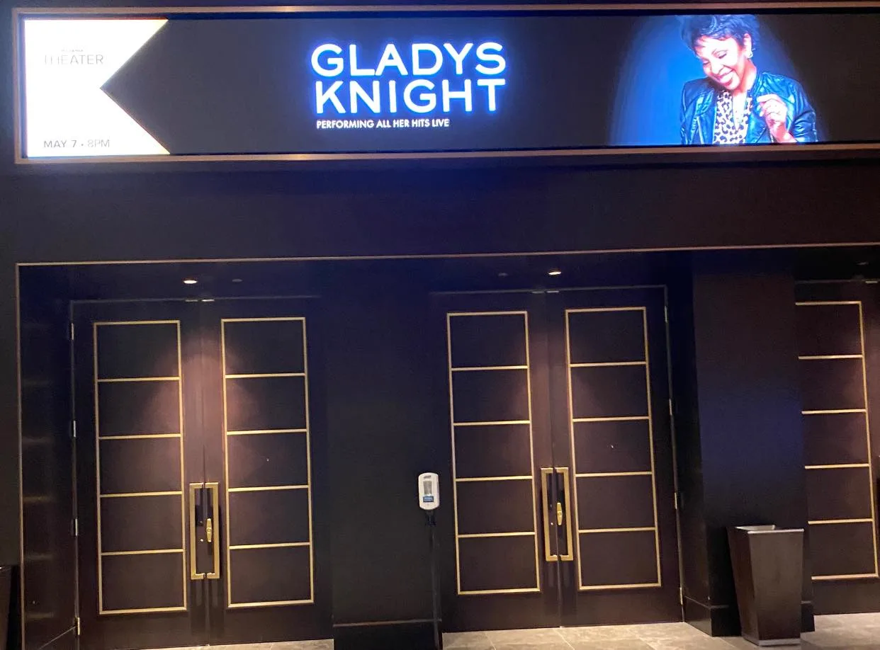 Theater entrance with dark double doors trimmed in gold, beneath a lit marquee reading "Gladys Knight – Performing All Her Hits Live, May 7, 8PM" with her photo.