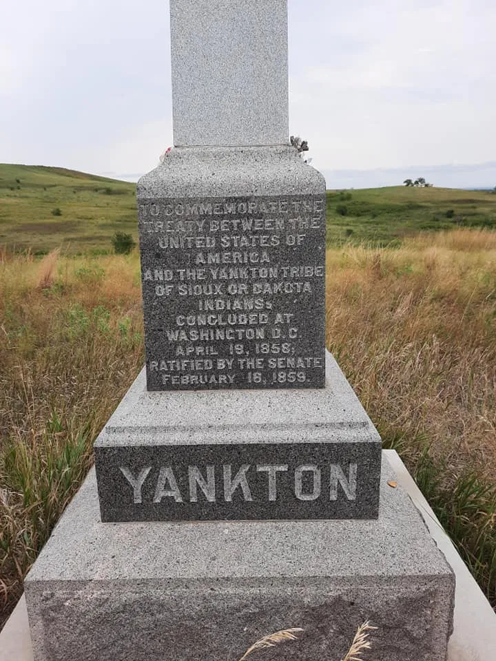Gray granite monument on a grassy prairie hill, inscribed to commemorate the treaty between the United States and the Yankton Sioux, concluded April 19, 1858, with YANKTON carved on the base.