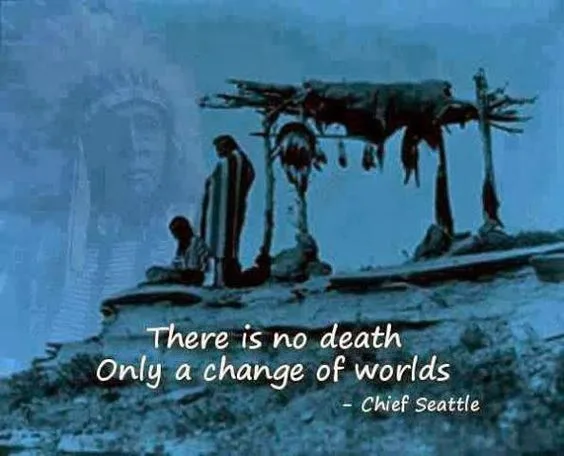 Blue-tinted image of two figures in blankets on a rocky hilltop beside a burial scaffold, a ghostly elder in a feather headdress above, with the quote "There is no death, only a change of worlds" by Chief Seattle.