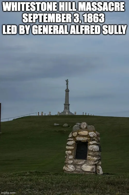 A stone cairn with a dark plaque stands on a grassy hill below a tall monument topped by a figure, under grey skies. Text reads: Whitestone Hill Massacre, September 3, 1863, led by General Alfred Sully.