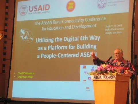 Chief Phil Lane Jr. speaks at a podium in Hanoi before a large screen reading "Utilizing the Digital 4th Way as a Platform for Building a People-Centered ASEAN" at the ASEAN Rural Connectivity Conference.