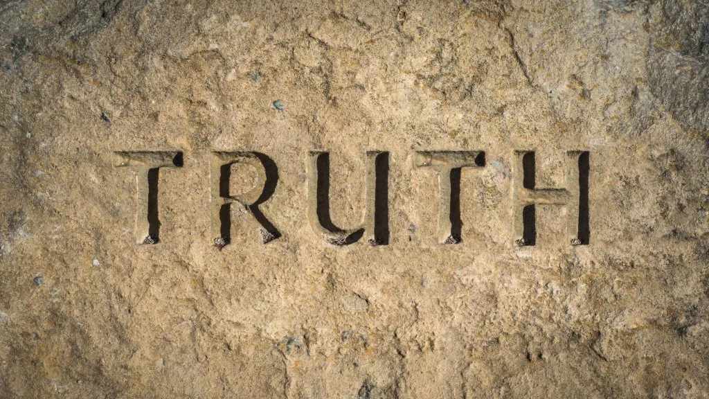 The word "TRUTH" carved in capital letters into a weathered, sunlit tan stone surface.